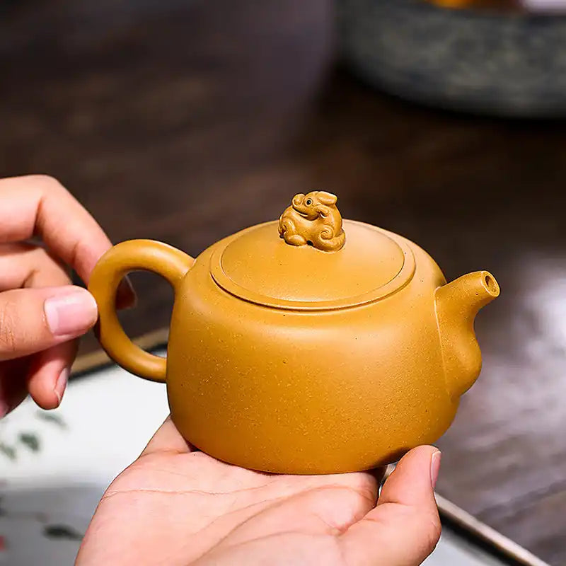 Yellow-brown ceramic teapot with a lion-shaped lid handle.