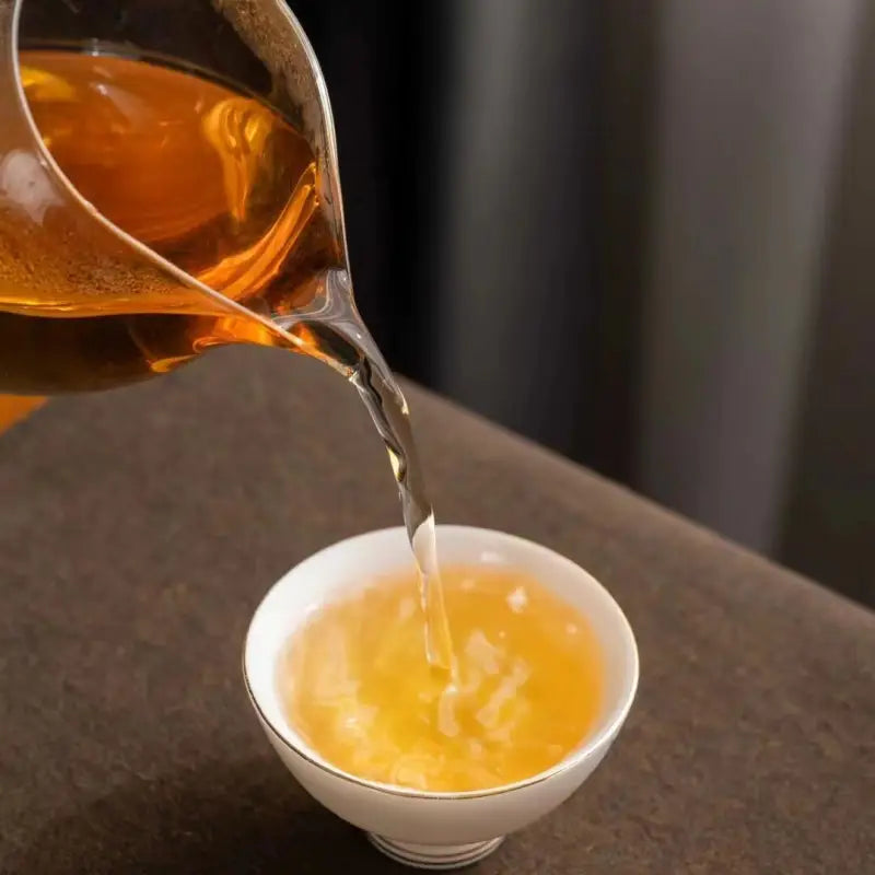 Pouring tea into a white cup showcasing 2014 Aged Shoumei Dark Aroma Edition white tea