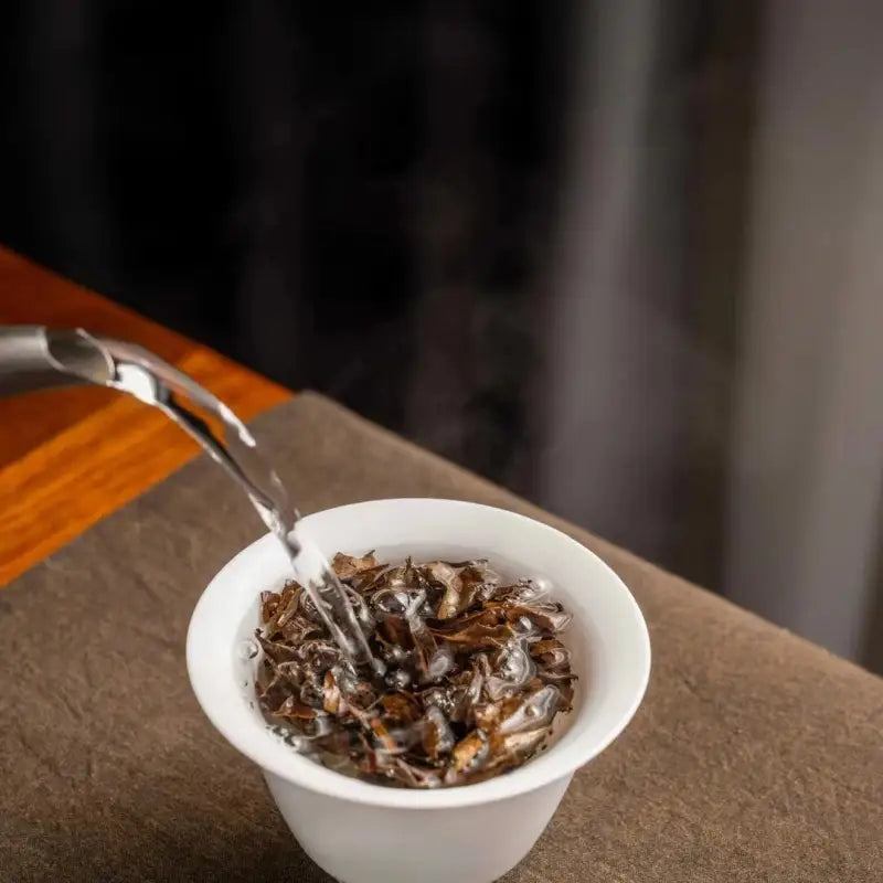 Pouring tea into a white cup featuring 2014 Aged Shoumei Dark Aroma Edition white tea
