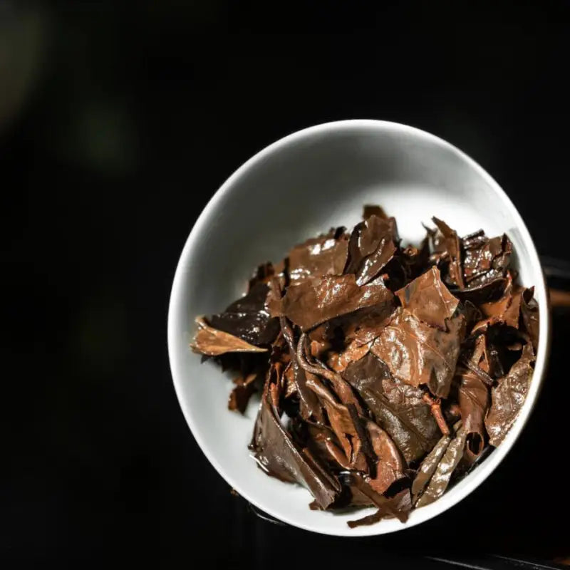 Loose dark fuding shoumei white tea leaves in a white bowl for aged white tea flavor