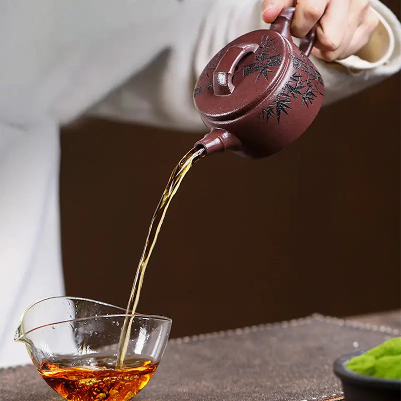 Maroon Yixing Zisha teapot pouring tea from Bamboo Elegance hand-carved bamboo design