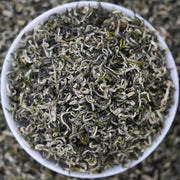 Bowl of dried Bi Luo Chun Green Tea Leaves with teapots and tea sets in background