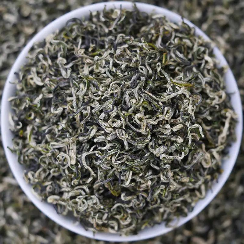 Bowl of dried Bi Luo Chun Green Tea Leaves with teapots and tea sets in background
