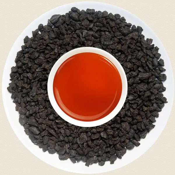 Black garlic surrounding red liquid with teapots and tea sets in the background