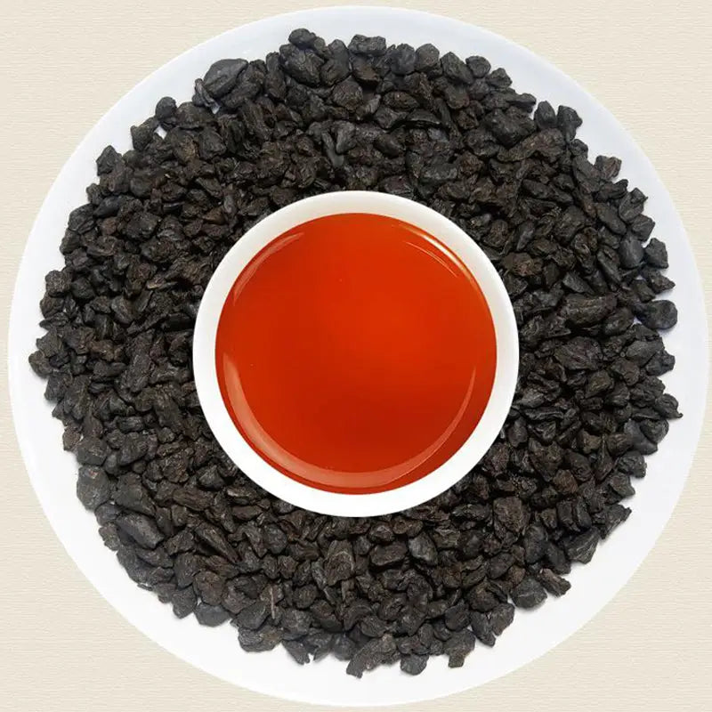 Black garlic surrounding red liquid with teapots and tea sets in the background