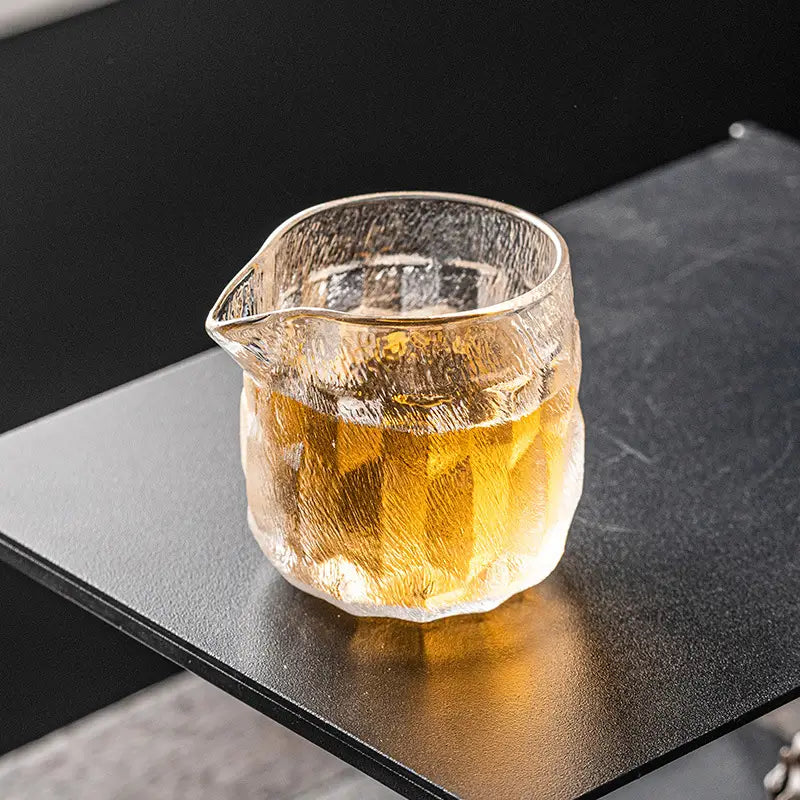 Handcrafted glass tea creamer in cloud mist textured glass filled with amber gongfu tea