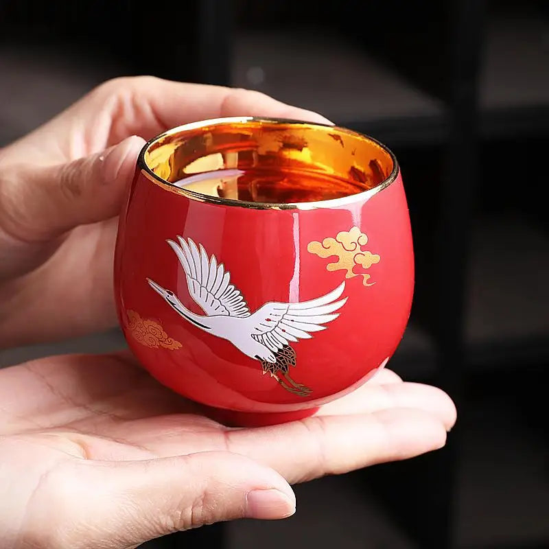 Red ceramic cup with flying white crane design, gold trim, and jian zhan style