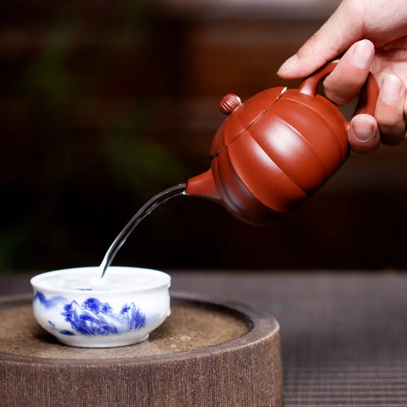 Reddish-brown Yixing Zisha teapot pouring water into a blue and white teacup for Crimson Harvest