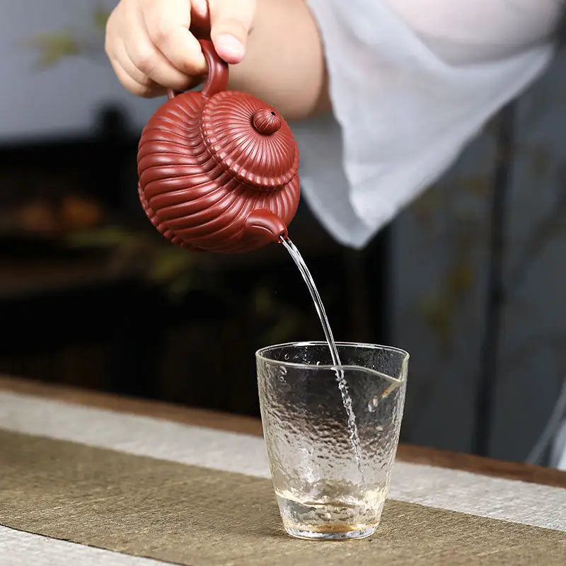 Red-brown ribbed yixing zisha teapot pouring into textured glass in Crimson Spiral harmony