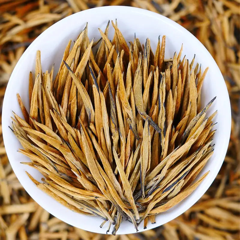 Golden needle tea leaves for Da Jin Zhong Black Tea displayed with teapots and mugs