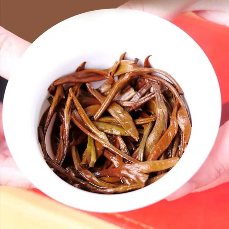 Loose reddish-brown tea leaves for Da Jin Zhong Black Tea in teapots and mugs
