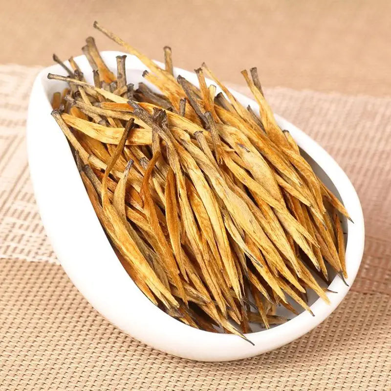 Golden tea leaves in a white bowl for Da Jin Zhong Black Tea Leaves with teapots and mugs