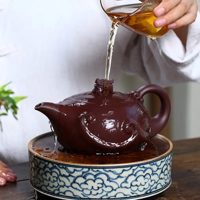 Elaborate brown Dragon Crest teapot being filled, showcasing sculpted dragon Yixing Zisha craftsmanship