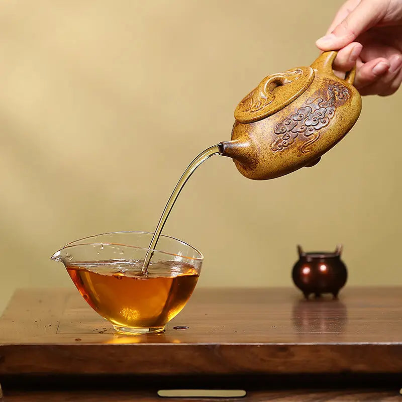 Ornate brown Yixing teapot with dragon carvings pouring tea, made from Duanni clay