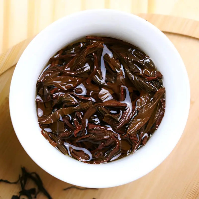 Infused dark Tea Leaves in a white bowl for Floral Sou Chong Red Tea served with teapots