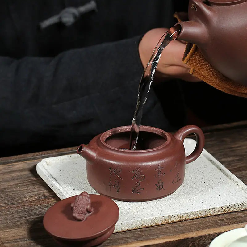 Earthenware Fortune Toad Yixing Zisha Teapot being filled for authentic tea brewing