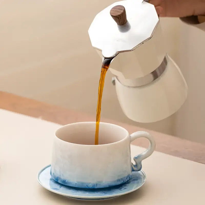 Coffee being poured into a Frosted Dawn Ceramic Coffee Cup with tenmoku glaze and matching saucer