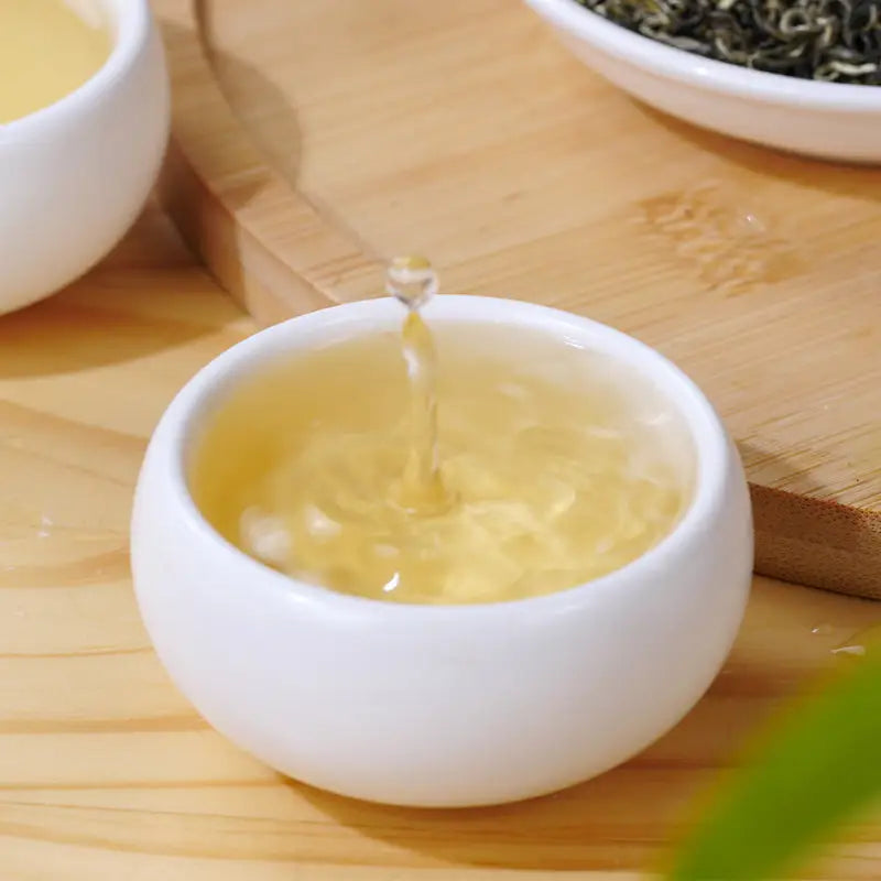 White teacup pouring liquid from a teapot, part of Gan Lu Piao Xue Jasmine Tea Leave set
