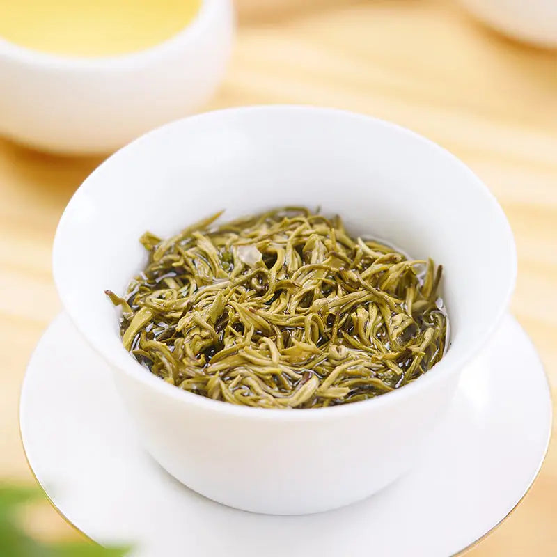 Green tea leaves in a white mug for Gan Lu Piao Xue Jasmine Tea Leaves with teapots