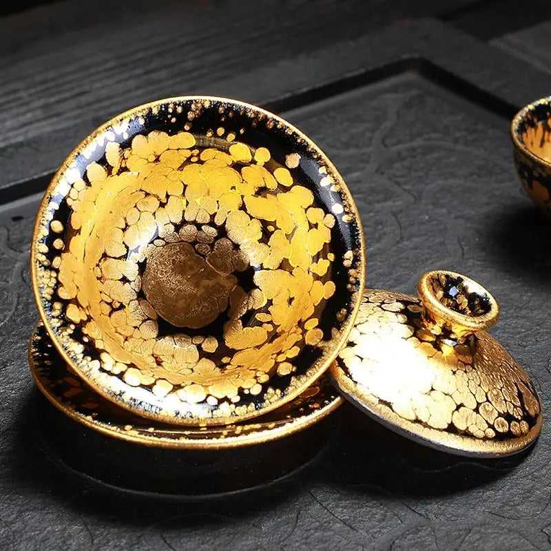 Black and gold tea set featuring a fairness pitcher and gold Jian Zhan tea accessories