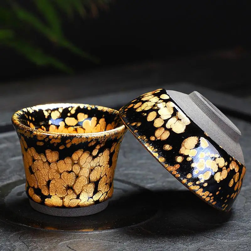 Two black and gold ceramic cups from the Gold Tea Set featuring Jian Zhan tea design