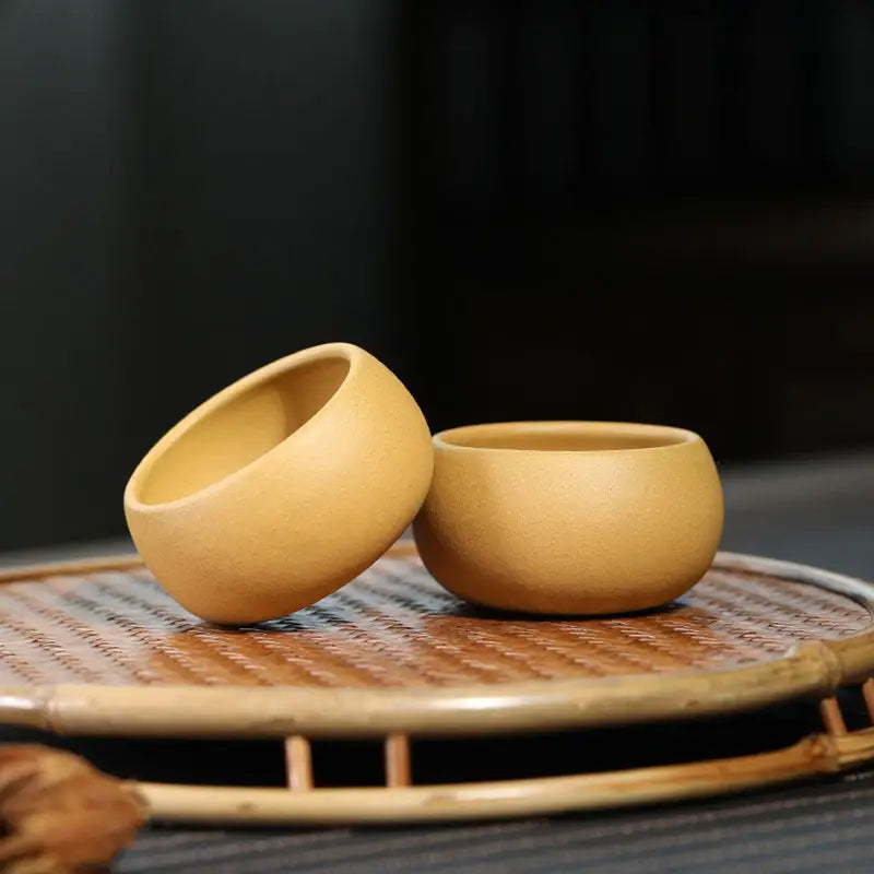 Two small round yixing zisha golden ember teacups in a gongfu tea set display
