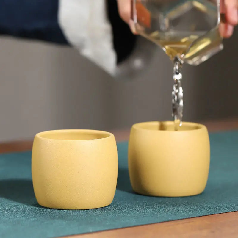 Yellow Duanni Clay ceramic cups from Golden Harmony, one filled with liquid for a refined tea experience