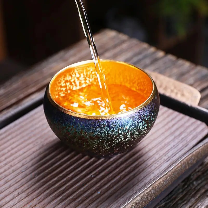 Iridescent tea cup being filled with Golden Magic jian zhan tea for a magical experience