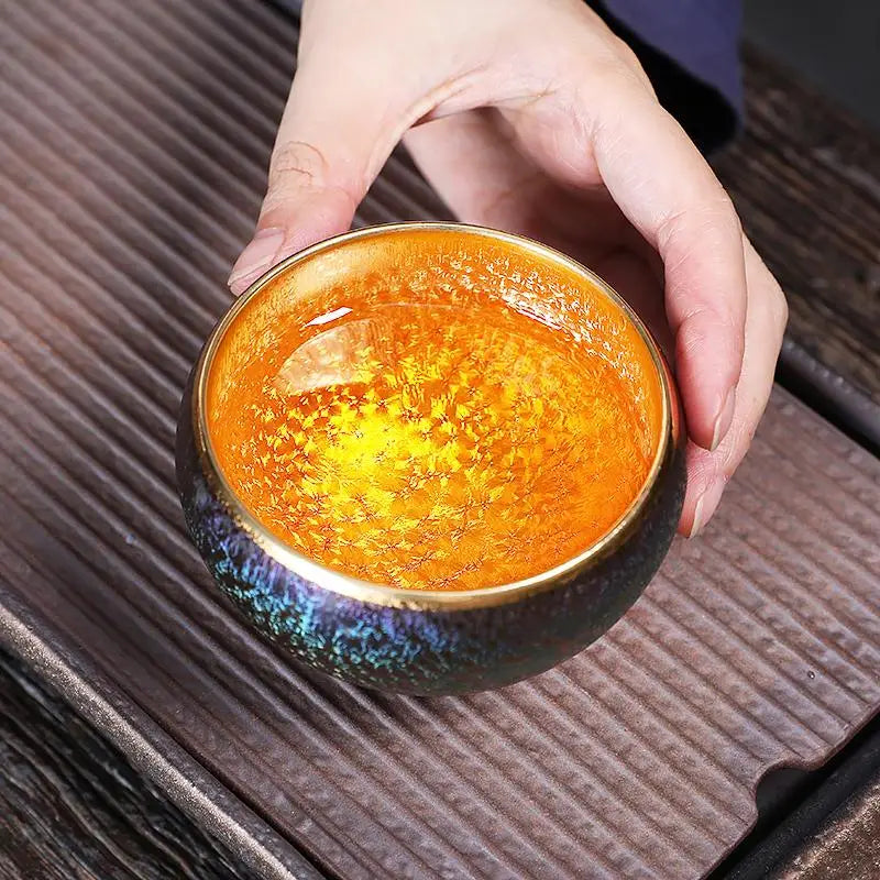 Iridescent tea cup with golden liquid from Golden Magic featuring Jian Zhan tea design