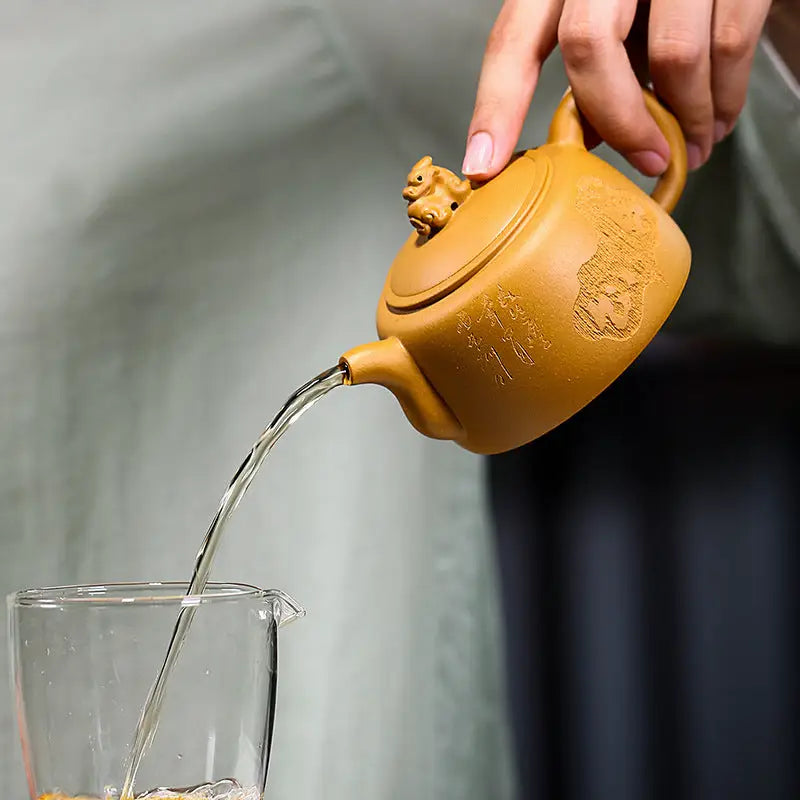 Earthenware Yixing teapot with guardian beast lid pouring liquid, crafted from golden Duanni clay