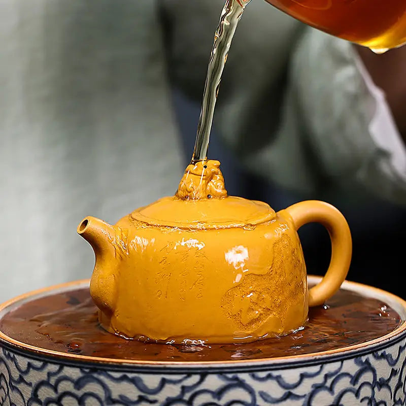 Yellow ceramic Yixing teapot with guardian beast lid made from golden Duanni clay being filled