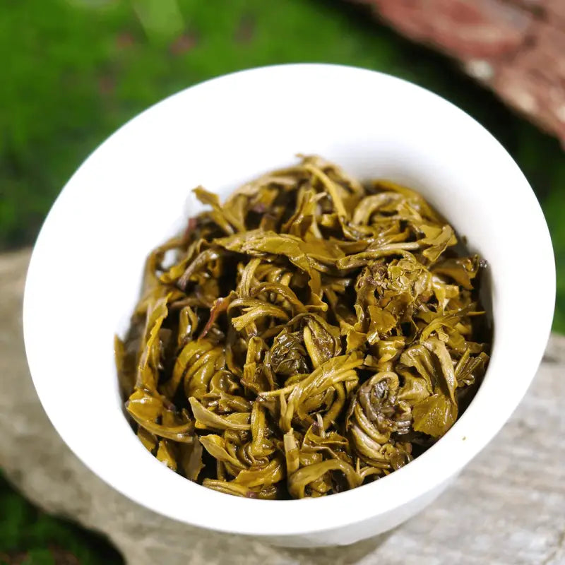 Steamed green tea leaves in a white bowl for Jasmine Dragon Ball Tea Leave with teapots and mugs