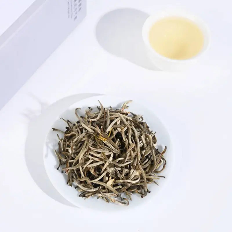 Pile of dried white tea leaves for Jasmine Silver Needle with fresh jasmine flowers