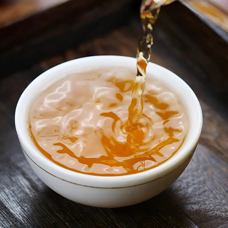 Tea being poured into a white bowl from Jin Luo Red Tea Leaves with teapots and tea sets