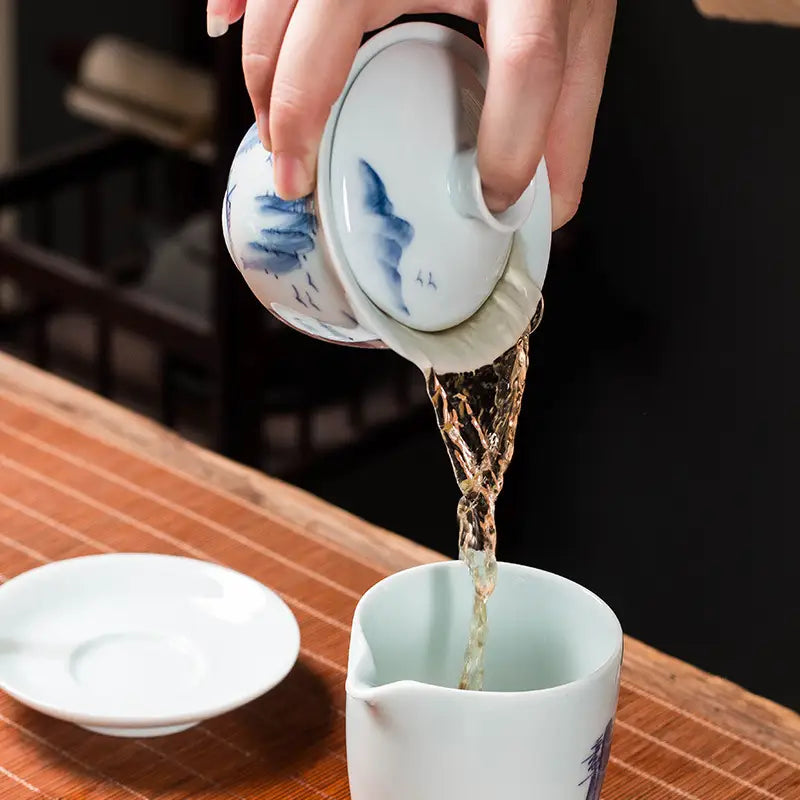 Tea pouring from a blue and white Gaiwan featuring mountain landscape enamel art
