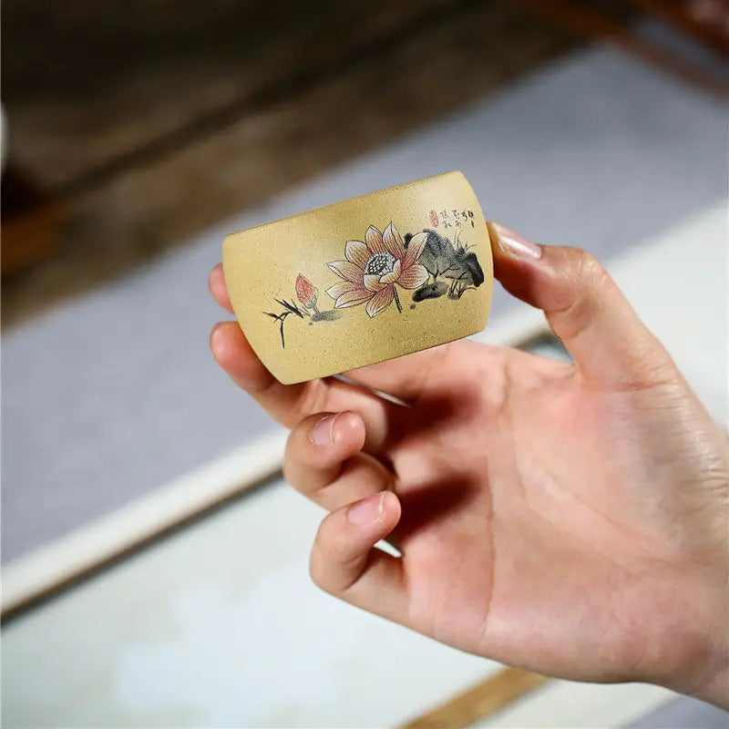 Hand-held tan-colored yixing zisha teacup with lotus flower design and poetic calligraphy
