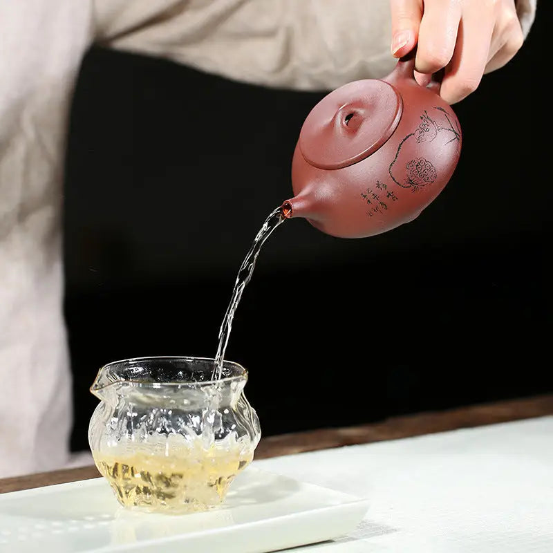 Brown Lotus Whisper Yixing teapot pouring liquid into glass cup with lotus pods