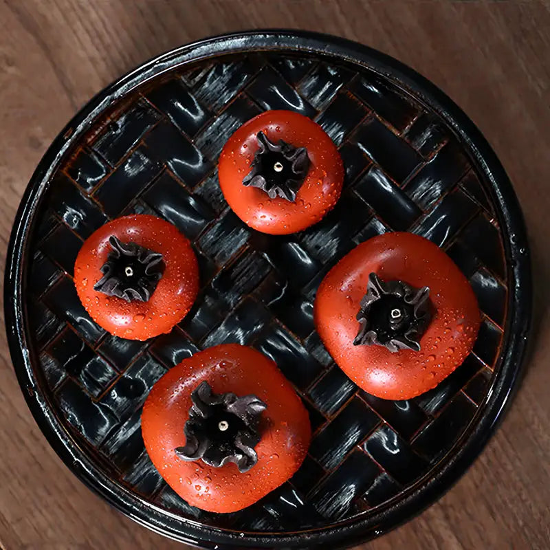 Four orange persimmons on a black woven tray for Lucky Persimmon tea pet display