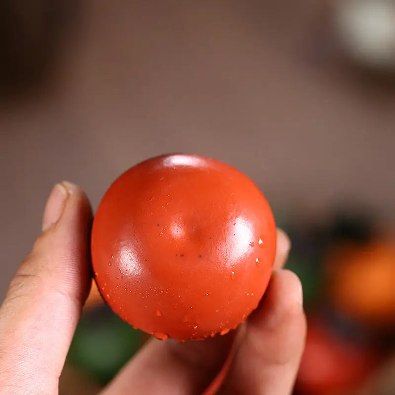 Round red ripe tomato next to Lucky Persimmon tea pet and Zisha clay tea pot
