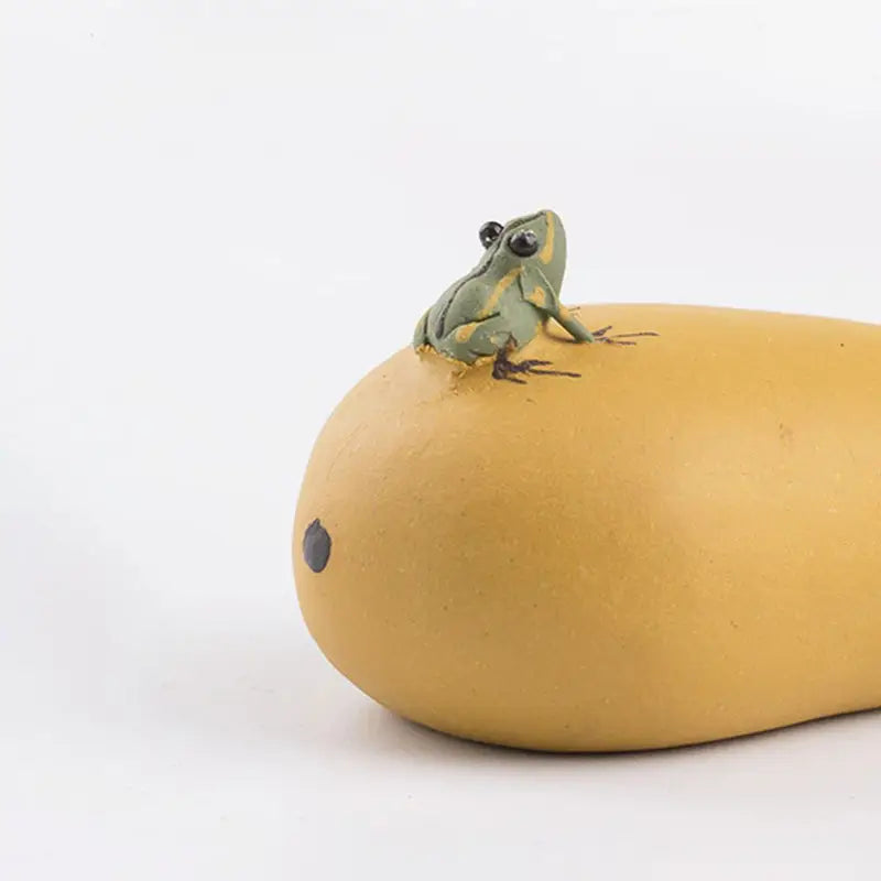Green frog on yellow mango tea pet showcasing charming tea and feng shui harmony
