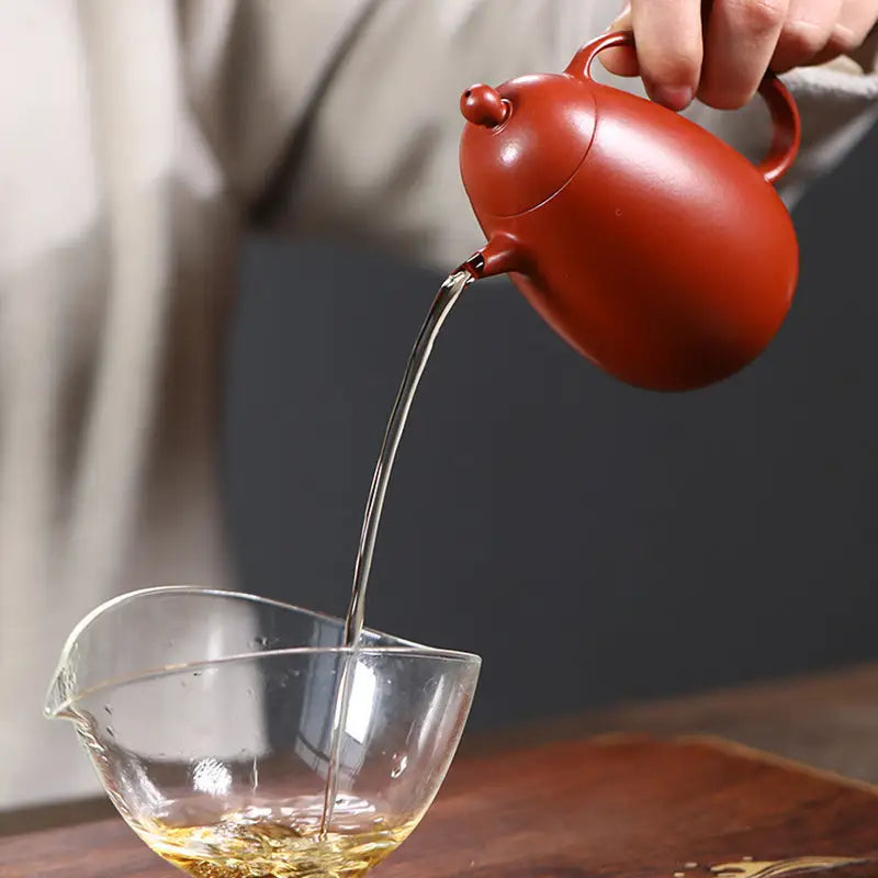 Reddish-brown Yixing teapot pouring tea showcasing Modern Simplicity design in red clay