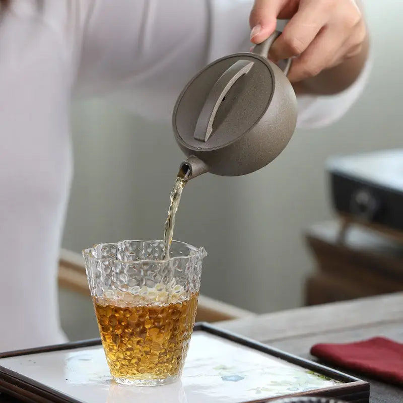 Tea being poured from a Moonbridge harmony teapot into a textured glass showcasing Zisha harmony Yixing craftsmanship