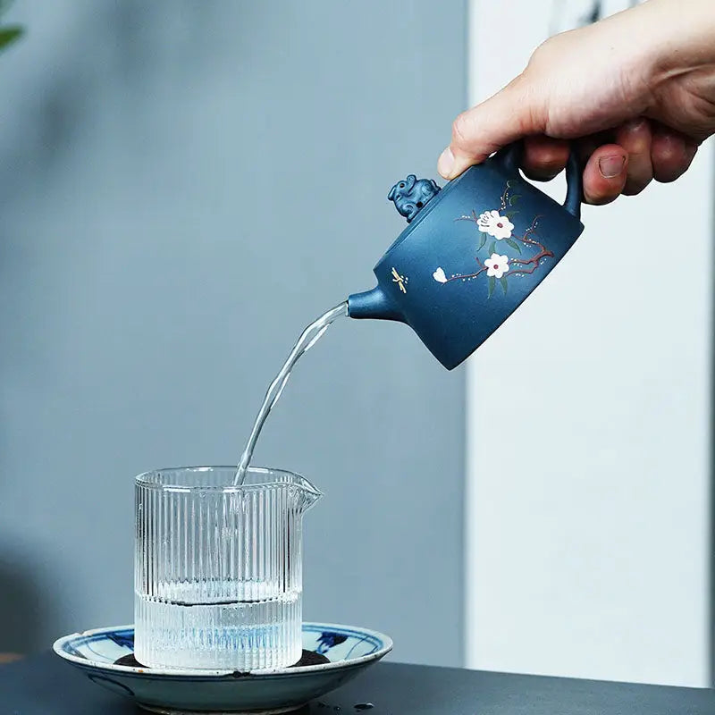 Floral-decorated blue Yixing Zisha teapot pouring water near Moonlit Guardian figurine