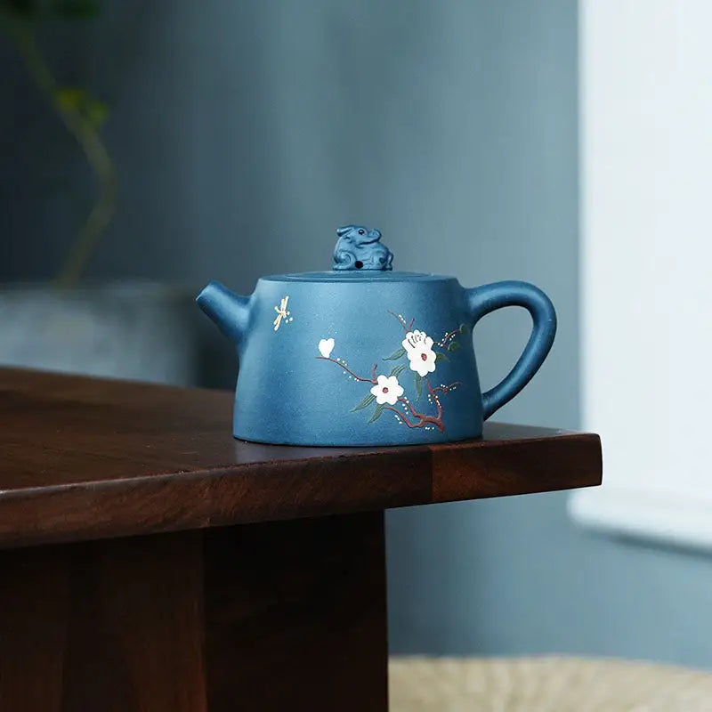 Blue ceramic teapot with floral design, inspired by Moonlit Guardian figurine, showcasing white plum artwork