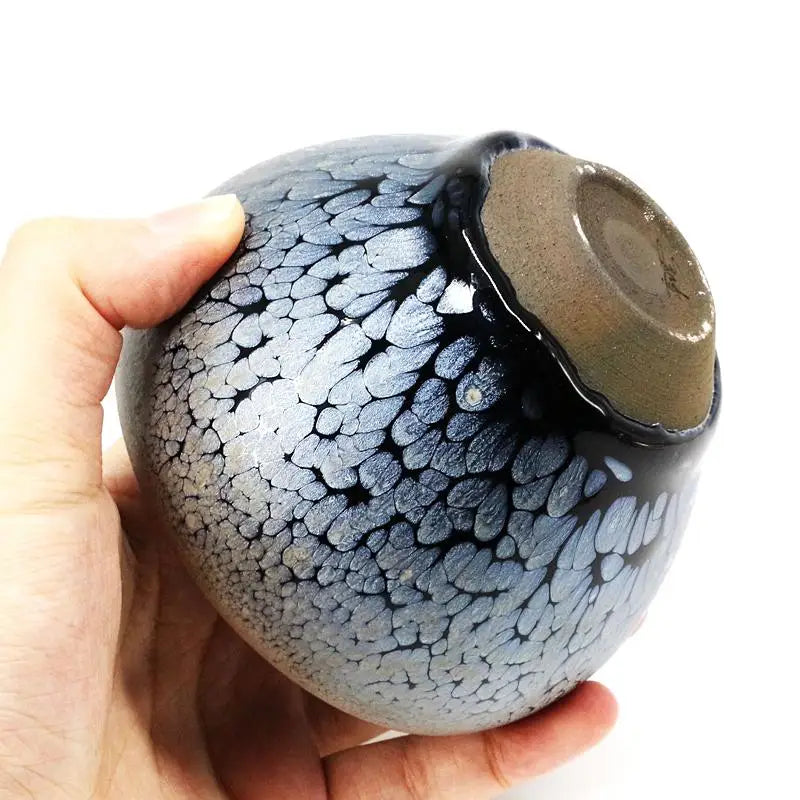 Hand holding a Nebula Jian Zhan gongfu tea cup with black and silver pattern