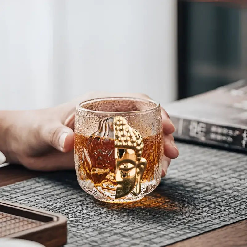 Textured glass cup with golden Buddha face showcasing spiritual symbolism and crackle glass teacup design