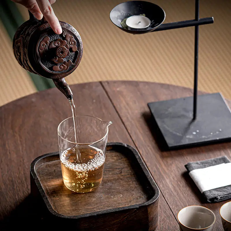 Relief Dragon teapot pouring tea into a glass pitcher, crafted from Jianshui Zitao clay