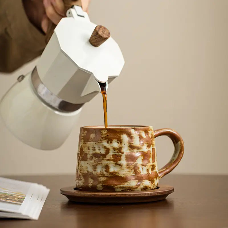 Coffee being poured into a Rust Coffee Cup made of handmade Dehua ceramic on a wood saucer