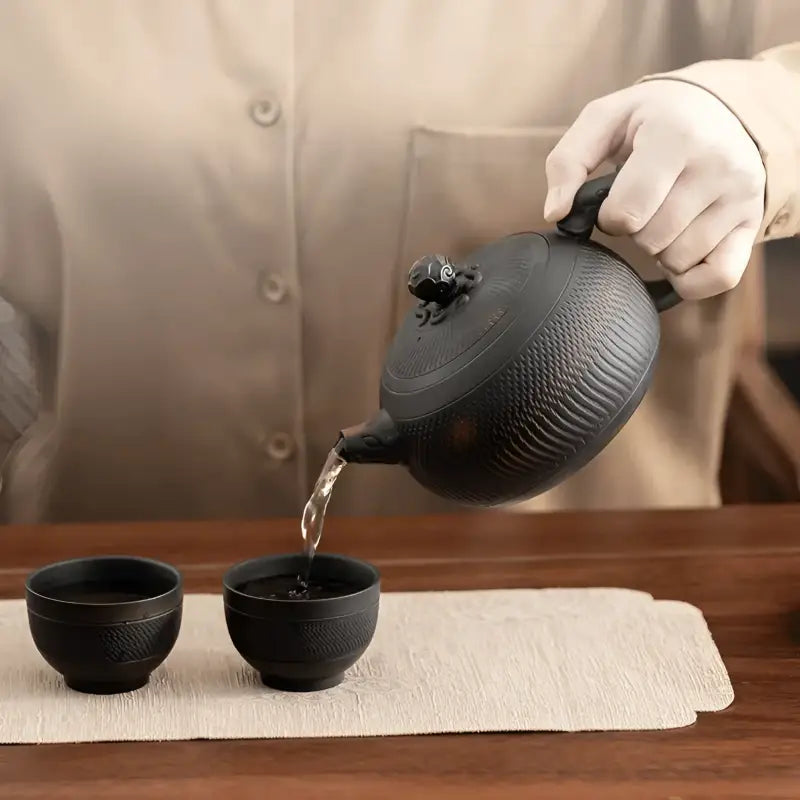 Textured black Shadow Lion Yixing Zisha teapot pouring tea from the Shadow Lion Tea Set
