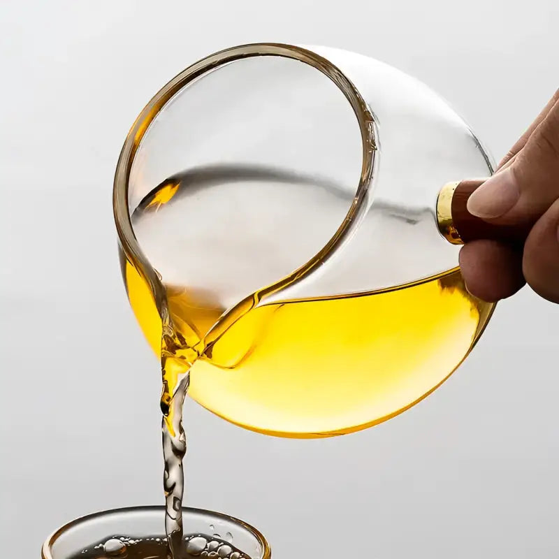 Glass tea pitcher with wooden handle pouring yellow liquid, borosilicate glass tea